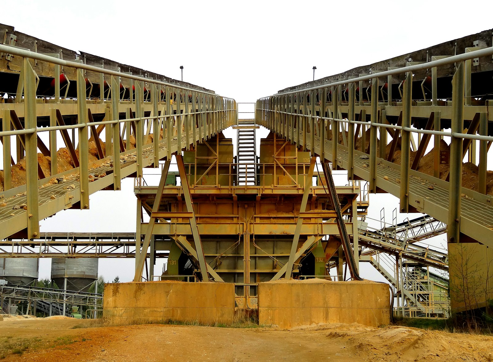 Two inclined belt conveyors carrying aggregate meet at a quarry processing structure